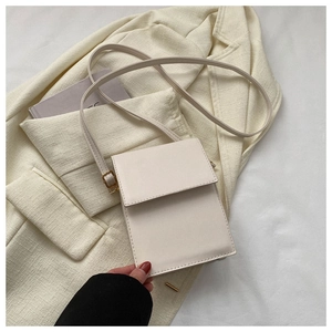 Détail d'un sac bandoulière en cuir PU blanc crème sur un blazer et un livre d'art