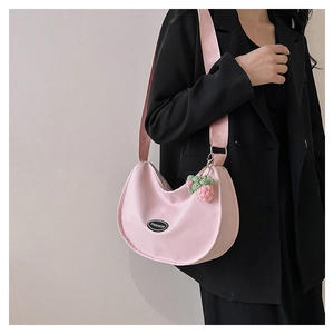 Detail of pink crescent bag with woven strawberry charm and wide shoulder strap