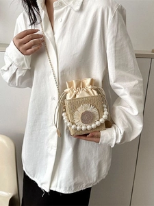 Handwoven straw crossbody bag with pearl handle and sunflower detail on white shirt