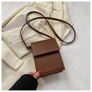 Vue détaillée d'un sac bandoulière minimaliste en cuir marron sur un blazer beige