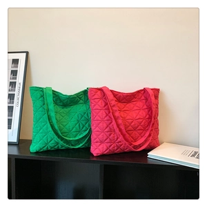 Close-up of quilted green and pink nylon tote bags displayed on a black wooden shelf