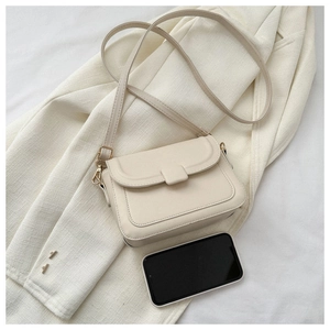 Close-up of a cream crossbody bag with phone for size comparison on a white blazer