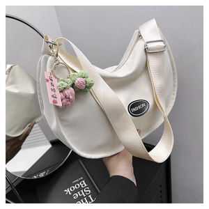 Detail of ivory canvas crescent bag with fashion tag and knitted flower pendant accessory