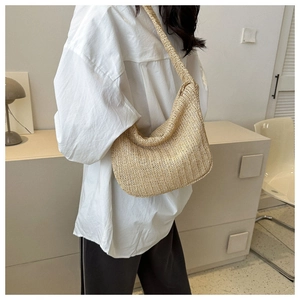 Side view of woman carrying a hand-woven crescent straw shoulder bag in minimalist room