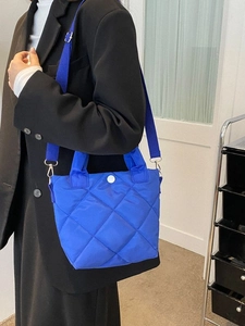 Minimalist blue quilted nylon handbag with crossbody strap worn by a model in black blazer