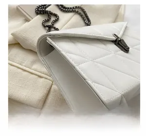 Détail d'un sac bandoulière blanc matelassé avec fermoir trapèze gris et bandoulière chaîne