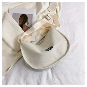 Detailed view of cream nylon crescent shoulder bag on beige blazer and fashion magazine