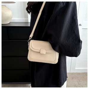 Detail shot of a beige leather crossbody square bag featuring a flap closure and matching buckle