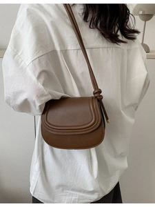 Brown minimalist semi-circle saddle bag with knot detail worn by a model in casual setting