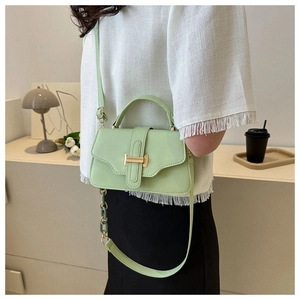 Close-up of a light green crossbody bag with a gold H-shaped buckle on a model