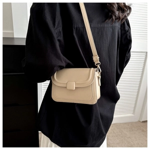 Detail of a beige flap crossbody bag with matching decorative square buckle and gold hardware