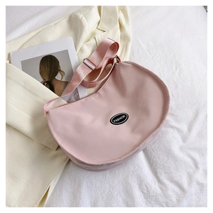 Detail of pink crescent bag with adjustable strap and fashion badge on textured fabric