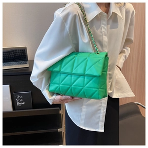 Dettaglio borsa trapuntata verde brillante con catena indossata da una modella in ufficio