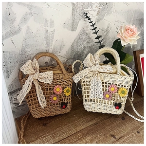 Detail of handmade woven straw bags with white lace bows and floral accents in a rustic setting