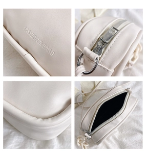 Close-up of cream leather crossbody bag featuring embossed fashion text and silver chain detail