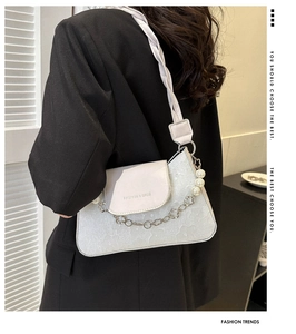 Detail of elegant white underarm bag featuring floral texture and pearl chain strap