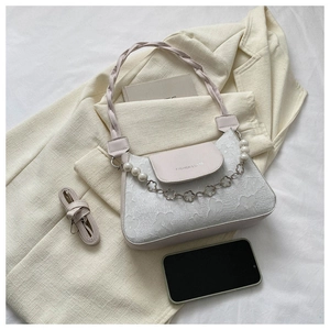 Detail of cream crossbody bag featuring floral embossing and pearl chain decoration