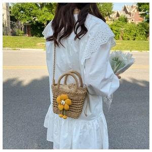 Detail of a woven straw bucket bag with sunflower charm and drawstring closure on a dress