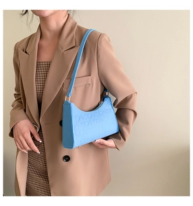 Detail of light blue felt bag showing geometric texture and gold metal buckle on shoulder strap