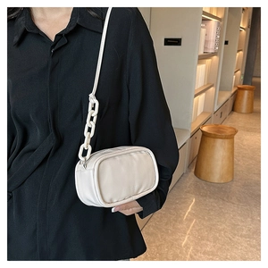 Detail of a creamy white mini crossbody bag with chain strap on a model's shoulder