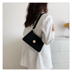 Model wearing black crocodile textured shoulder bag with a gold buckle in a minimalist setting