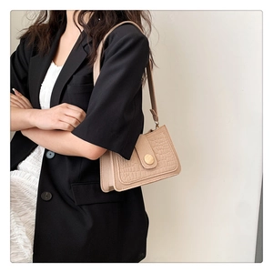 Detail of beige faux crocodile skin shoulder bag with gold hardware on a model