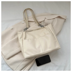 Detail view of beige faux leather tote bag featuring functional front pockets and metal chain