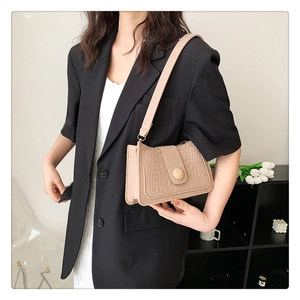 Close-up of beige crocodile pattern baguette bag with round wooden buckle on a model