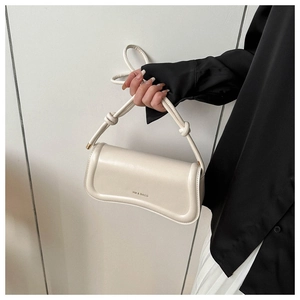 Detailed close-up of cream curved leather handbag with knot strap and gold accents