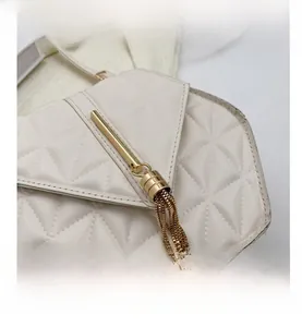 Close-up of beige quilted crossbody bag featuring a unique gold tassel hardware detail