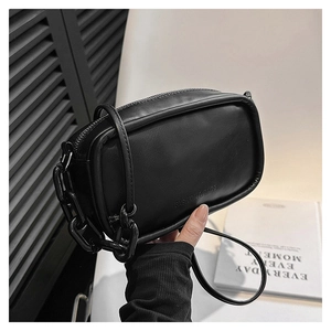 Close-up of black leather crossbody bag featuring a chunky chain and embossed logo