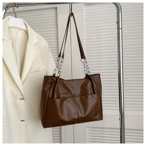 Detail of dark brown tote bag with metal chains and large front pockets on a rack