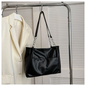 Detail of black PU tote bag with silver chain handles and front pockets on a blazer