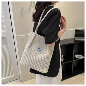 Detail of cream-colored knit tote bag featuring bubble texture and decorative logo patch