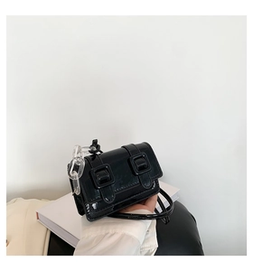 Detail of glossy black satchel bag with double buckle straps and acrylic chain strap