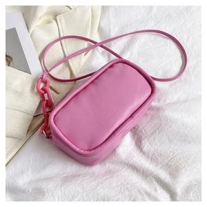 Detail of peach pink faux leather crossbody bag with resin chain on white fabric