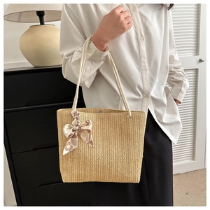 Détail du sac cabas en paille beige avec anses en corde tressée et nœud en soie élégant
