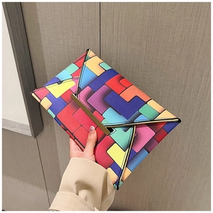 Detail of colorful geometric puzzle envelope clutch with golden metal bar and cross-grain texture