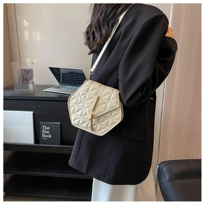 Close-up of cream quilted crossbody bag with gold tassel on a black blazer
