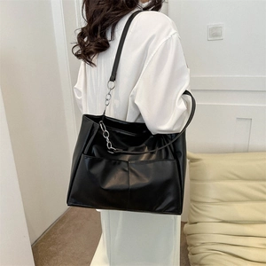 Minimalist large black tote bag with silver chain strap worn by a model in casual setting