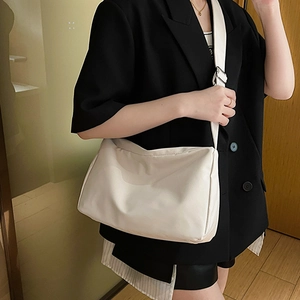 Minimalist beige nylon crossbody bag with adjustable strap worn over a black blazer
