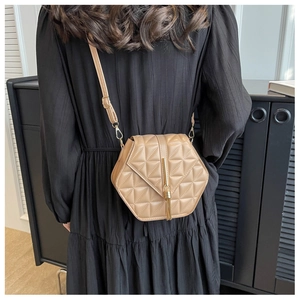 Detail of light brown hexagonal crossbody bag featuring quilted patterns and a tassel charm