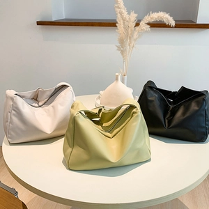 Three minimalist soft leather tote bags in cream, green, and black shown on a table