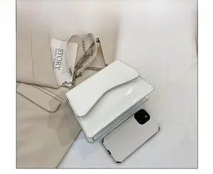 Detailed top view of white patent leather shoulder bag with chain strap and phone for scale