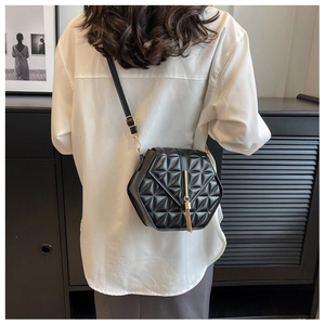 Detail showing hexagonal quilted leather crossbody bag with golden tassel on white shirt