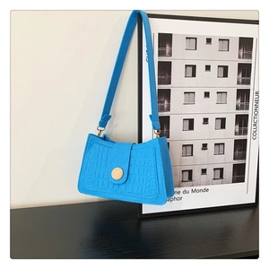 Detail of bright blue faux leather shoulder bag featuring crocodile texture and wood button