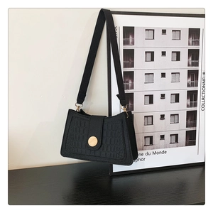 Detail of black faux crocodile leather underarm bag with gold metal buckle and wide strap