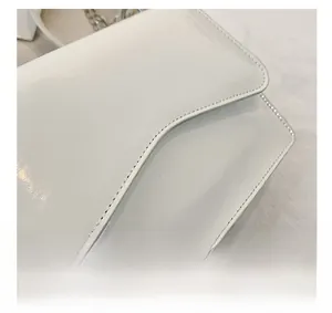 Close-up of white glossy patent leather finish and silver chain strap detail on a bag