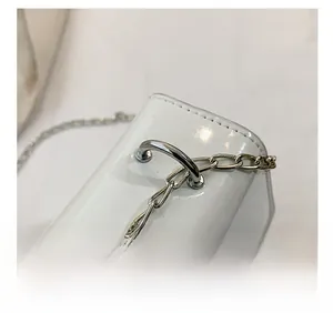 Close-up of white patent leather bag with silver D-ring hardware and flat metal chain detail