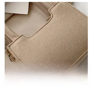 Detail of premium beige felt fabric with precise stitching and gold metal buckle on handbag
